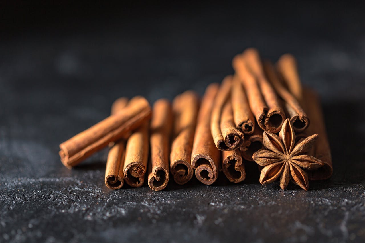 hero-img-02 Close-up of cinnamon sticks and star anise on a dark, textured surface, evoking warm, aromatic flavors.