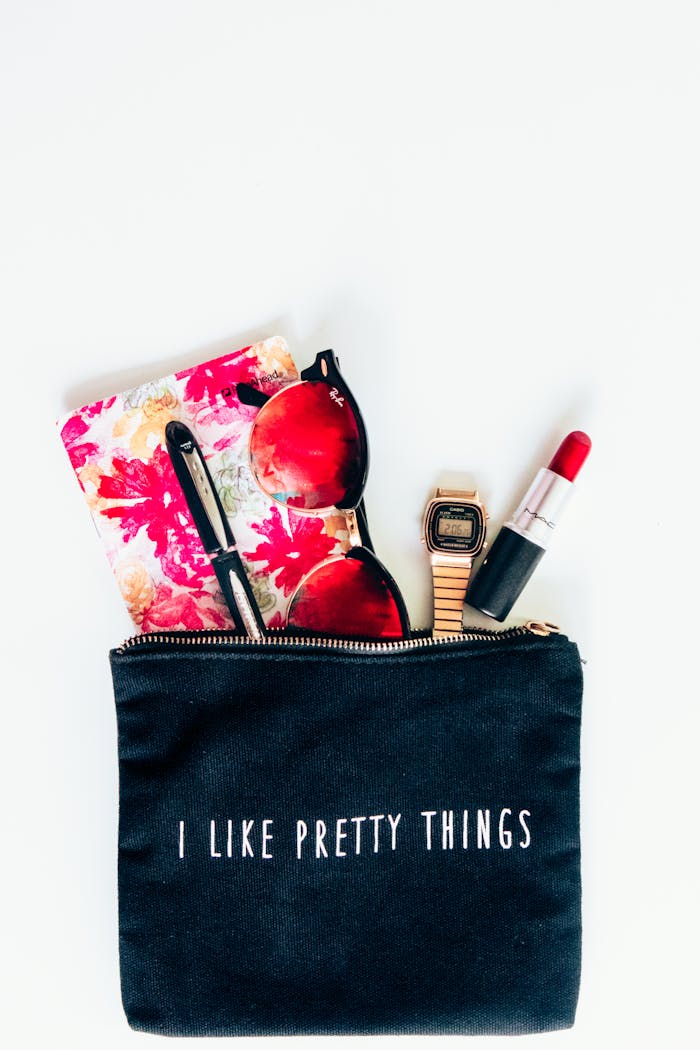 A flat lay of fashion accessories including sunglasses, lipstick, and a watch with a bold pouch.