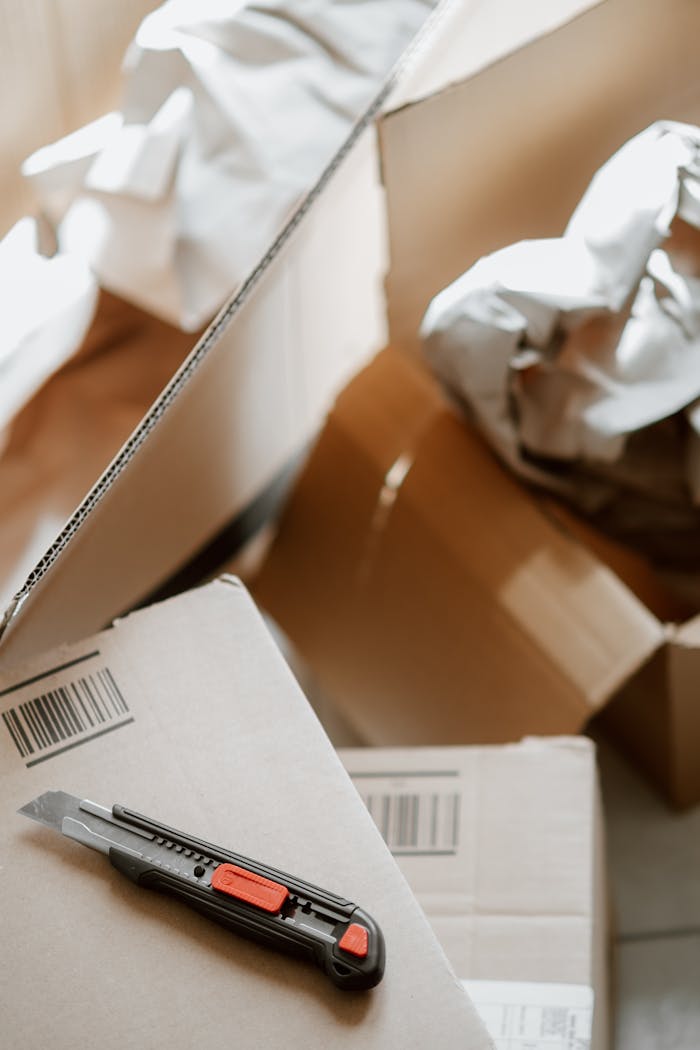 From above of utility knife on heap of carton boxes with crumpled papers during relocation