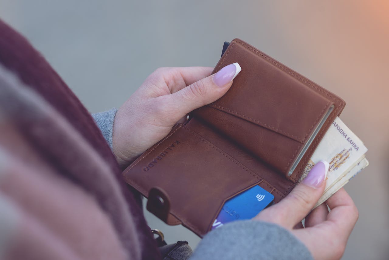 Close-up image of hands holding a brown leather wallet with banknotes and a credit card visible.