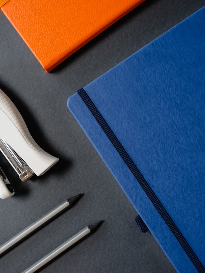 gallery-4 Close-up view of colorful notebooks, pens, and a stapler on a dark surface, ideal for office themes.